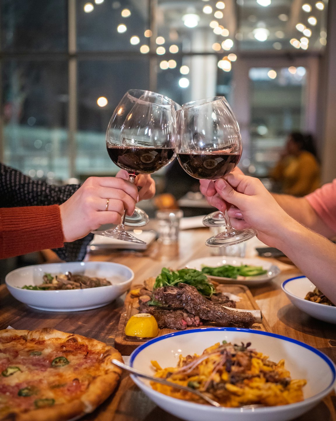Dos personas brindando con copas de vino tinto durante una comida.